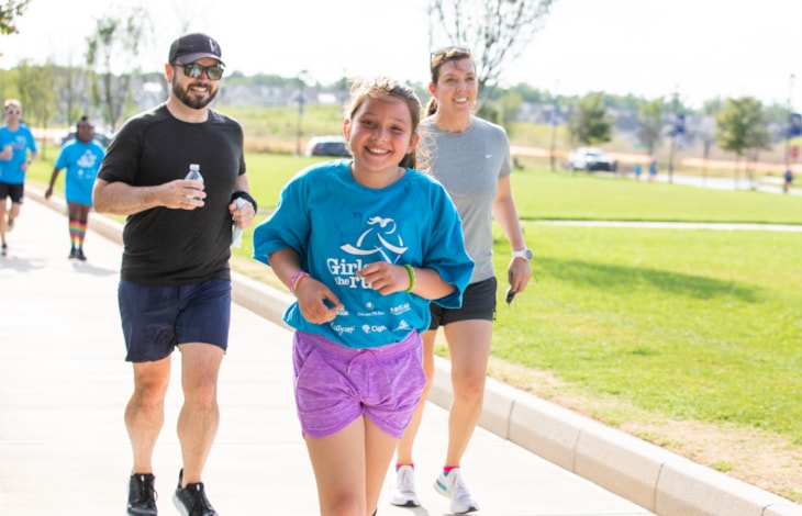 A Girls on the Run participant smiles next to a caregiver as they look down at a journal. A Girls on the Run participant smiles next to a caregiver as they look down at a journal.